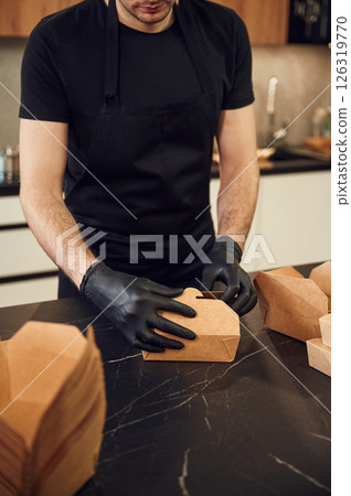 On the table. Man is packing food into the paper eco boxes. Indoors, restaurant On the table. Man is packing food into the paper eco boxes. Indoors, restaurant 126319770