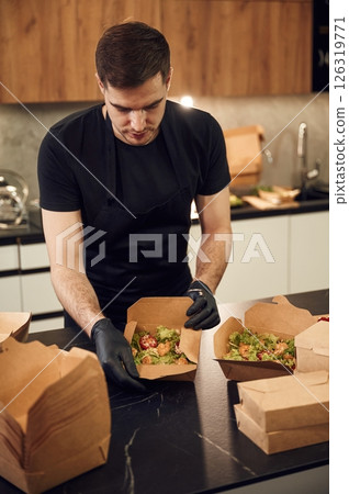 On the table. Man is packing food into the paper eco boxes. Indoors, restaurant On the table. Man is packing food into the paper eco boxes. Indoors, restaurant 126319771