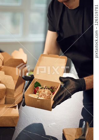 Fresh burger with vegetables. Man is packing food into the paper eco boxes. Indoors, restaurant Fresh burger with vegetables. Man is packing food into the paper eco boxes. Indoors, restaurant 126319781