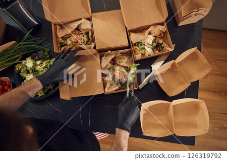 Top view. Man is packing food into the paper eco boxes. Indoors, restaurant Top view. Man is packing food into the paper eco boxes. Indoors, restaurant 126319792