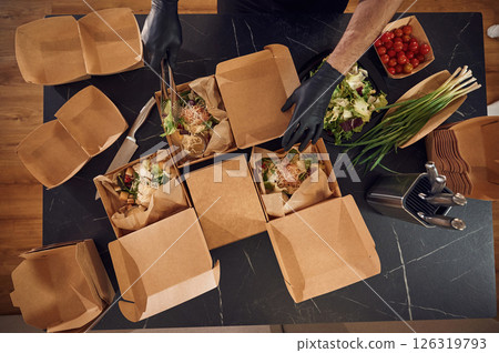 Top view. Man is packing food into the paper eco boxes. Indoors, restaurant 126319793
