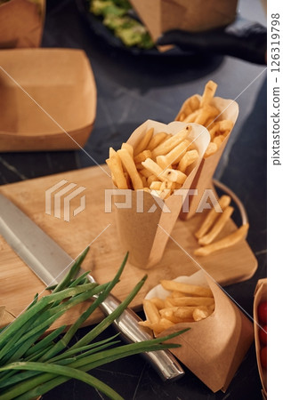 Close up view of French fries that are in the paper eco box. Green onion and knive on the table 126319798