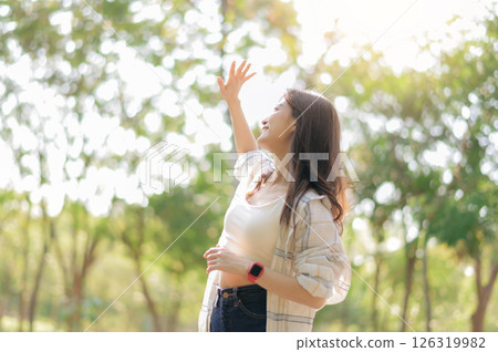 Southeast asian female young woman enjoying refreshing deep breath in public park expressing wellness and embracing healthy lifestyle in sunlight. young woman in casual attire enjoys sunny day outdoor 126319982