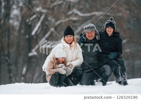 Sitting and looking forward. Happy family is outdoors, enjoying snow time at winter together Sitting and looking forward. Happy family is outdoors, enjoying snow time at winter together 126320190