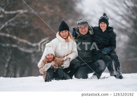 Sitting and looking forward. Happy family is outdoors, enjoying snow time at winter together Sitting and looking forward. Happy family is outdoors, enjoying snow time at winter together 126320192