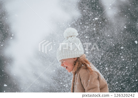 Happy little girl is enjoying winter snowfall outdoors 126320242
