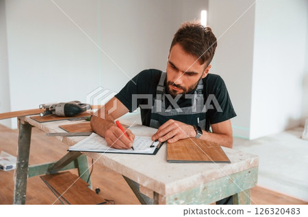 Man sitting by the table and writing data into notebook. With new laminated wooden floor Man sitting by the table and writing data into notebook. With new laminated wooden floor 126320483