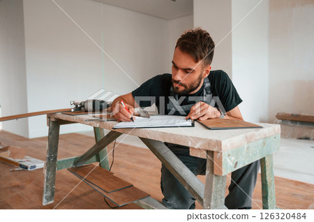 Man sitting by the table and writing data into notebook. With new laminated wooden floor 126320484