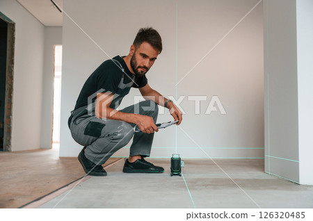 Sitting and making measurements by using laser leveler. Man is installing new laminate wooden floor Sitting and making measurements by using laser leveler. Man is installing new laminate wooden floor 126320485