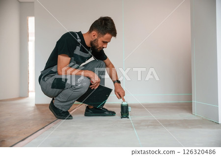 Sitting and making measurements by using laser leveler. Man is installing new laminate wooden floor 126320486