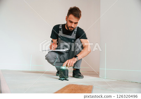 Laser leveler device. Man is installing new laminated wooden floor Laser leveler device. Man is installing new laminated wooden floor 126320496