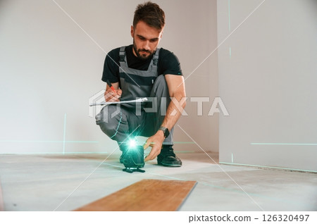 Laser leveler device. Man is installing new laminated wooden floor Laser leveler device. Man is installing new laminated wooden floor 126320497