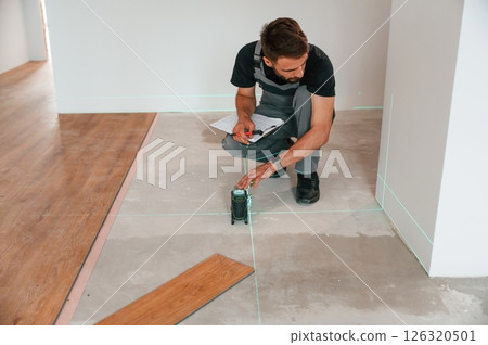Using the device that shows straight lines by laser. Man is installing new laminated wooden floor Using the device that shows straight lines by laser. Man is installing new laminated wooden floor 126320501