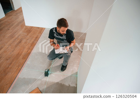 Using the device that shows straight lines by laser. Man is installing new laminated wooden floor 126320504