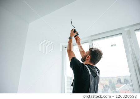 Installing lighting equipment on the ceiling. Man is working indoors at domestic room 126320558