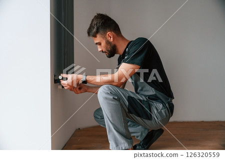 Plumber worker installing heating radiator in empty room of a newly built house 126320559