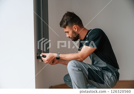Plumber worker installing heating radiator in empty room of a newly built house Plumber worker installing heating radiator in empty room of a newly built house 126320560