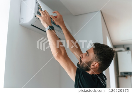 Man repairs an air conditioner indoors at home Man repairs an air conditioner indoors at home 126320575