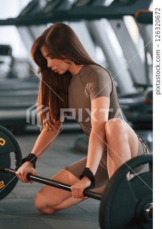 With barbell on the floor. Beautiful woman with sport body type is in the gym With barbell on the floor. Beautiful woman with sport body type is in the gym 126320672