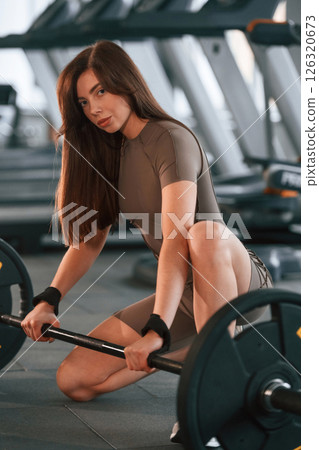 With barbell on the floor. Beautiful woman with sport body type is in the gym With barbell on the floor. Beautiful woman with sport body type is in the gym 126320673