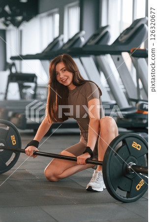 Barbell is on the floor. Beautiful woman with sport body type is in the gym 126320677