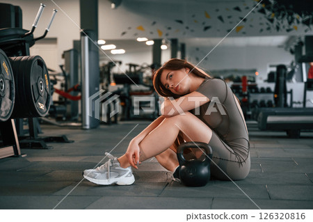 Sitting on the floor with dumbbell on it. Beautiful woman with sport body type is in the gym Sitting on the floor with dumbbell on it. Beautiful woman with sport body type is in the gym 126320816
