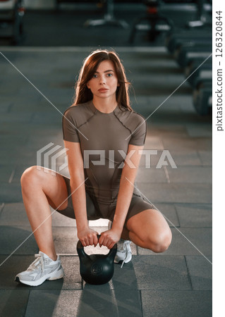Sitting on the floor with dumbbell on it. Beautiful woman with sport body type is in the gym Sitting on the floor with dumbbell on it. Beautiful woman with sport body type is in the gym 126320844