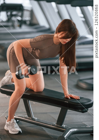 Hands exercises. Lifting dumbbell. Beautiful woman with sport body type is in the gym 126320868