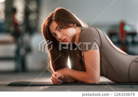Lying down on the yoga mat and resting. Beautiful woman with sport body type is in the gym Lying down on the yoga mat and resting. Beautiful woman with sport body type is in the gym 126320879