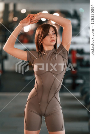 With hands up. Standing and posing. Beautiful woman with sport body type is in the gym 126320894