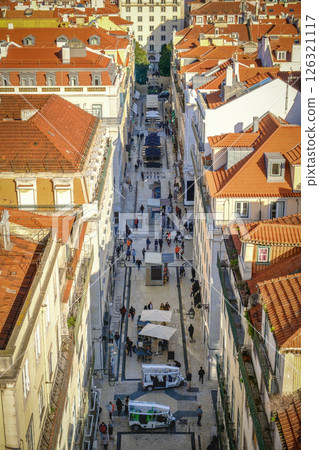 Overhead perspective of busy pedestrian street lined with historic buildings and red-tiled rooftops, people walking, touristic tuk-tuks, traditional pavement and outdoor cafes, vibrant atmosphere of 126321117