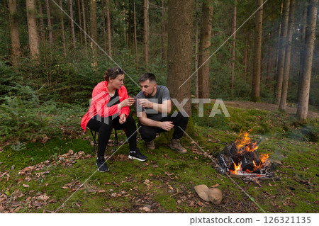 Outdoor adventure shared between two friends enjoying a warm campfire in the serene forest during an early evening 126321135
