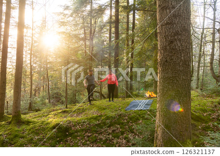 Couple enjoying a romantic walk in a serene forest at sunset, surrounded by lush greenery and soft golden light filtering through trees 126321137