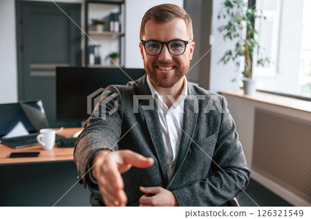 Giving the hand, greetings gesture. Businessman in suit is in the office with computer 126321549