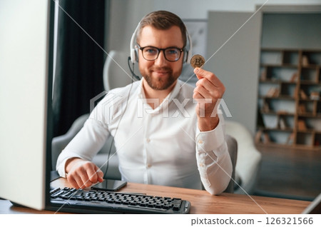 Holding bitcoin in the hand. Man in formal clothes is working in the modern office. Using computer 126321566