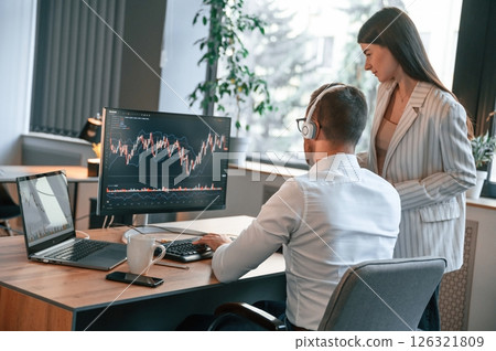 Two office workers are analyzing graphs that on the computer screen 126321809