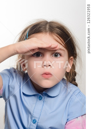 Young girl looking intently into the distance, shielding her eyes with her hand. 126321958