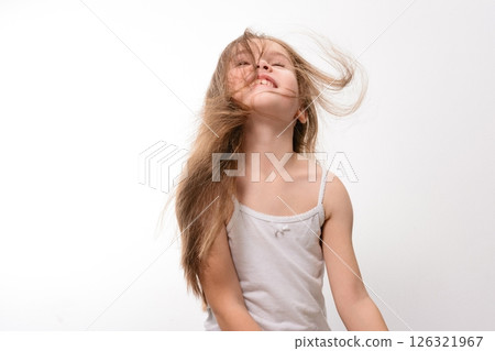 Joyful little girl with long hair playfully tossing her head back against a white background. 126321967