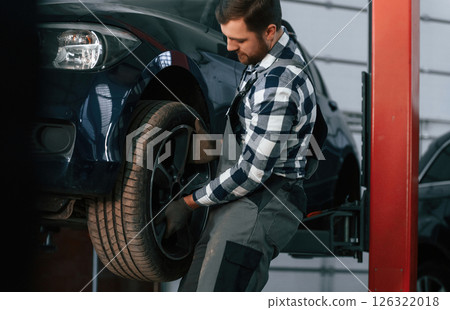 Holding and changing new tire. Man in uniform is working in the auto salon 126322018