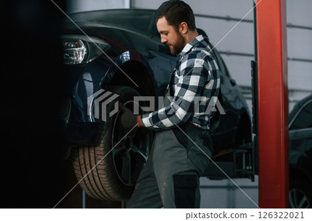 Holding and changing new tire. Man in uniform is working in the auto salon Holding and changing new tire. Man in uniform is working in the auto salon 126322021