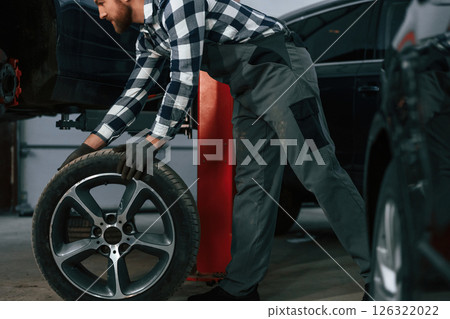 Moving the new tire for a car. Man in uniform is working in the auto salon Moving the new tire for a car. Man in uniform is working in the auto salon 126322022