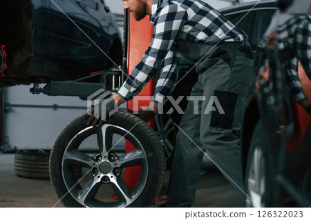 Moving the new tire for a car. Man in uniform is working in the auto salon Moving the new tire for a car. Man in uniform is working in the auto salon 126322023