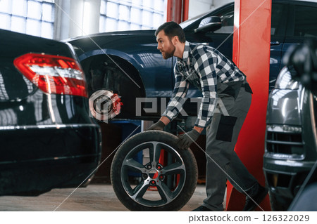 Side view. Moving the tire for the car. Man in uniform is working in the auto salon 126322029