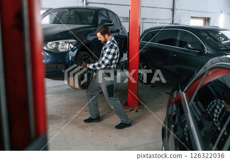 Front left wheel is changing. Man in uniform is working in the auto salon Front left wheel is changing. Man in uniform is working in the auto salon 126322036