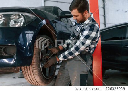Front left wheel is changing. Man in uniform is working in the auto salon Front left wheel is changing. Man in uniform is working in the auto salon 126322039