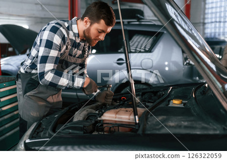 Repairing the electronics of the car under the hood. Man in uniform is working in the auto salon Repairing the electronics of the car under the hood. Man in uniform is working in the auto salon 126322059