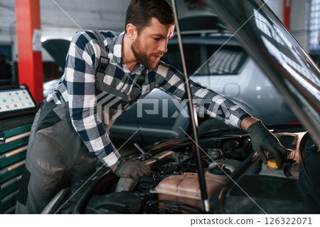 Focused on work. Repairing the car. Man in uniform is in the auto salon Focused on work. Repairing the car. Man in uniform is in the auto salon 126322071
