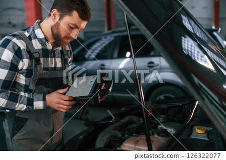With tablet in hands. Man in uniform is working in the auto salon With tablet in hands. Man in uniform is working in the auto salon 126322077