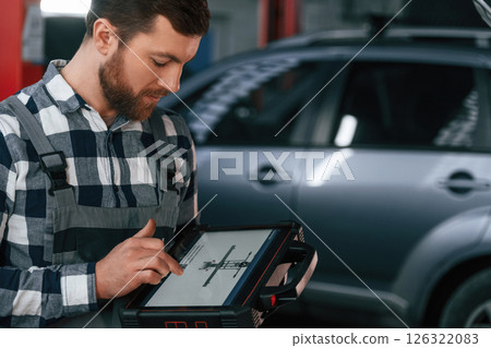 Graphic information is on the tablet. Man in uniform is working in the auto salon Graphic information is on the tablet. Man in uniform is working in the auto salon 126322083