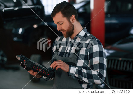 Holding tablet. Man in uniform is working in the auto salon 126322140